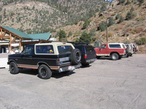 1996 Ford Bronco - A black and tan Ford Bronco is parked in front of a Starbucks with a mountain in the background. Several other SUVs are parked behind it.
