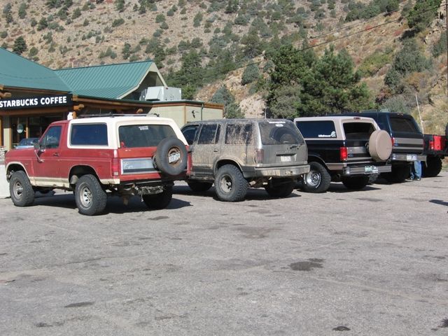 Red and white 1980s Ford Bronco parked at Starbucks, with other SUVs behind it.