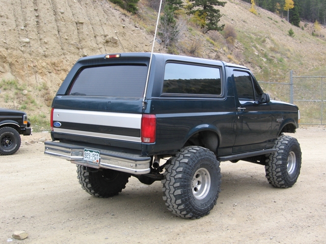 Lifted dark green 1996 Ford Bronco with large off-road tires, rear driver's side view.