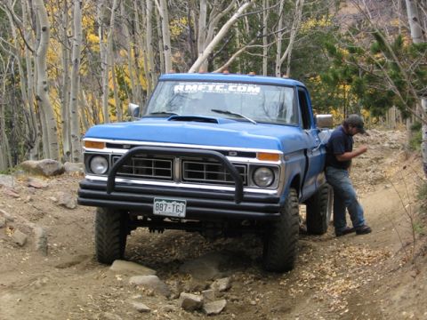 1996 Ford Bronco - A blue Ford pickup truck with a brush guard is parked on a dirt trail surrounded by trees. A man in jeans and a t-shirt leans against the d…