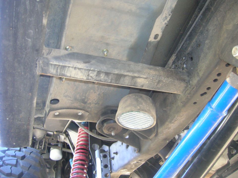 Underside of a vehicle frame with suspension parts and a light.