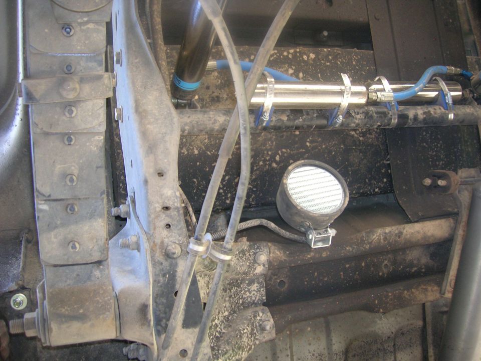 Underside of a vehicle showing suspension, light, and hydraulic cylinder.
