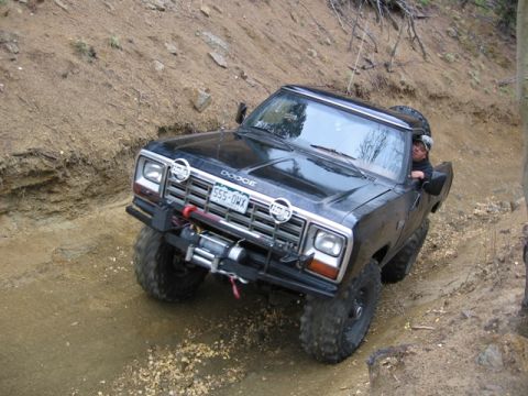 1996 Ford Bronco - A black Dodge pickup truck with large off-road tires navigates a steep, dirt trail. The truck is equipped with a winch on the front bumper…