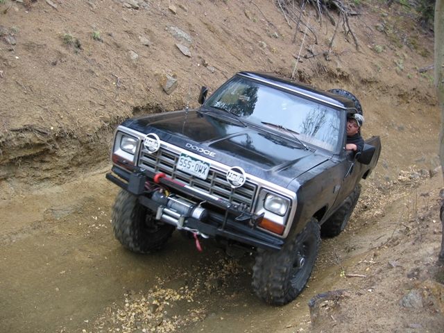 Black Dodge pickup truck with winch and large tires off-roading on a dirt trail.