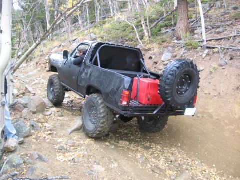 1996 Ford Bronco - A modified black pickup truck with large off-road tires navigates a rocky, wooded trail. The truck has a roll cage, a red jerry can, and a…