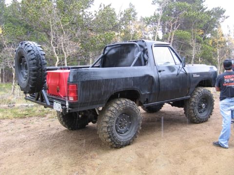 1996 Ford Bronco - The rear passenger side of a black, lifted Dodge Ramcharger is shown parked on a dirt road with trees in the background. The vehicle featur…