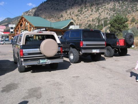 1996 Ford Bronco - The rear view of a lifted, dark-colored Ford Bronco is parked in front of a Starbucks. Another lifted Ford Bronco is parked to its right.