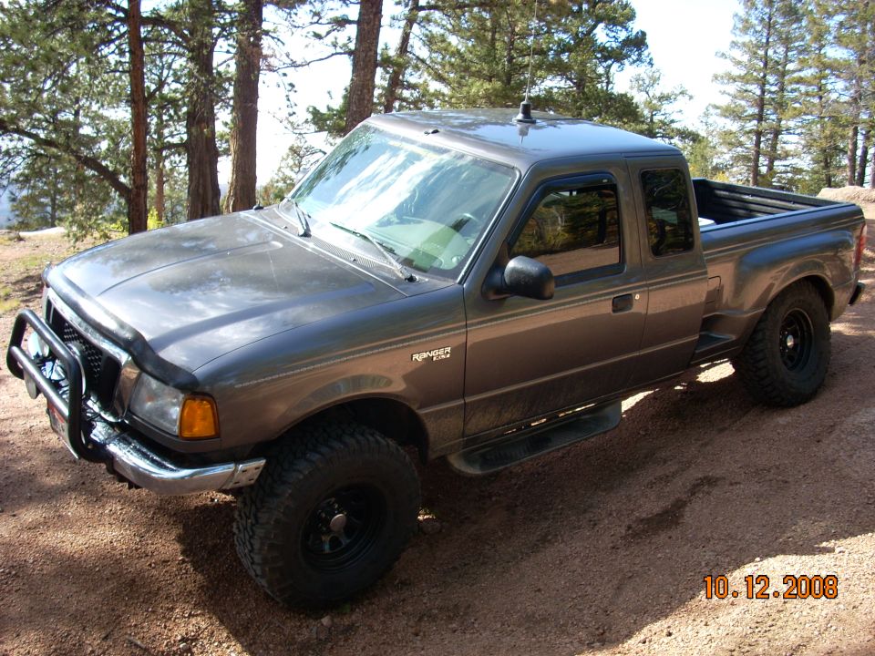 Dark gray Ford Ranger pickup truck with bull bar and off-road tires parked on a dirt road.