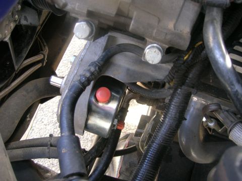 1996 Ford Bronco - A close-up view of a vehicle's engine bay, focusing on a hydraulic line connected to a component with a red button.