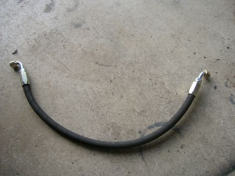 1996 Ford Bronco - A black hydraulic hose with silver fittings is laid out on a concrete surface. The hose is curved in a U-shape, with one fitting on the lef…
