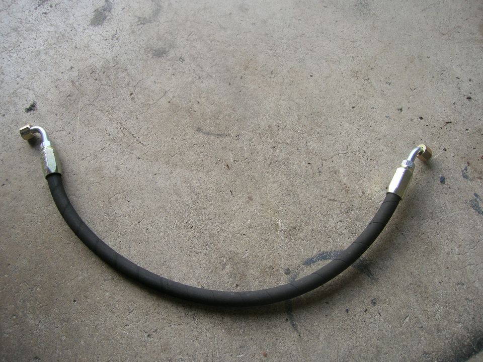 Black hydraulic hose with silver fittings on concrete.