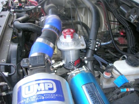1996 Ford Bronco - Close-up view of a modified engine bay, featuring a large UMP air intake system and a blue silicone intake hose connected to a turbocharger…