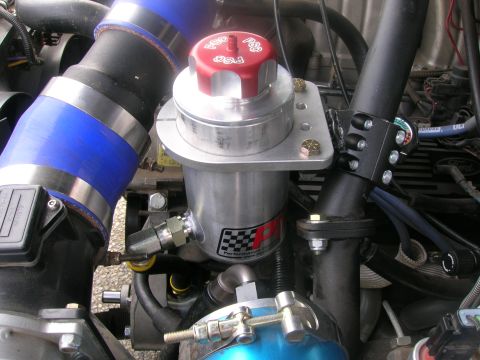 1996 Ford Bronco - A close-up view of a modified engine bay featuring a polished aluminum reservoir with a red cap and a black hose connected to a blue silico…