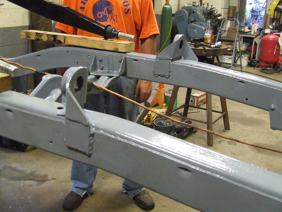 Gray painted vehicle frame with visible welds and mounting points, in a workshop.