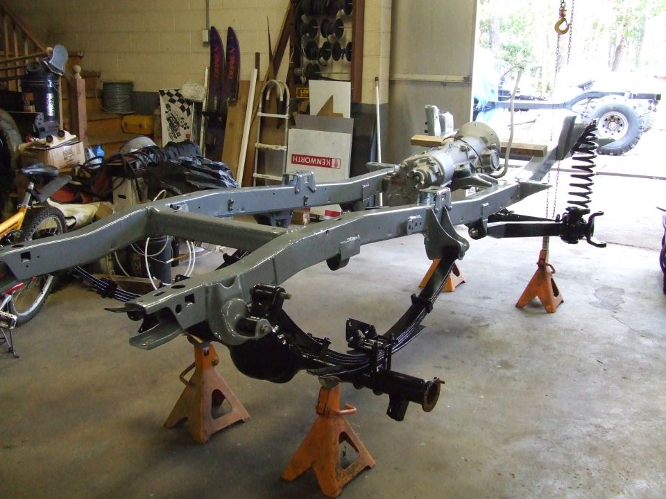 Vehicle frame with transmission and suspension on jack stands in a workshop.