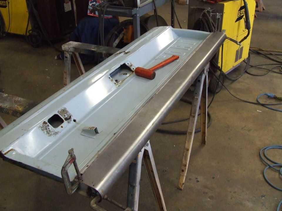 Car tailgate or door clamped to sawhorses with a hammer on top.
