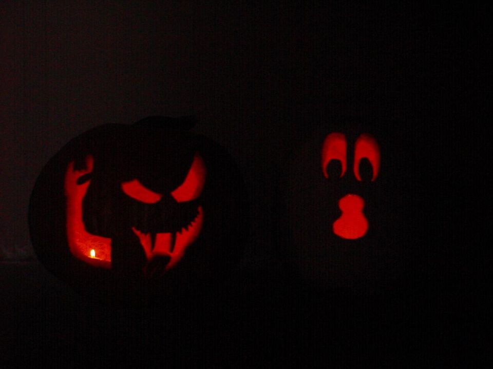 Two carved pumpkins with red light glowing from inside, one with a menacing face, the other with a ghost face.