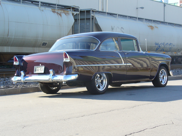 1955 Chevrolet sedan, rear 3/4 view, dark purple, custom wheels, train car background