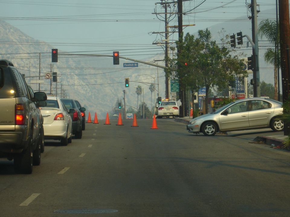 Traffic cones and a police car on a street with a silver sedan pulled over.