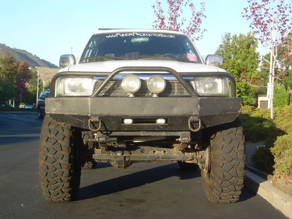 Front view of lifted white 4Runner with black steel bumper, bull bar, driving lights and mud tires