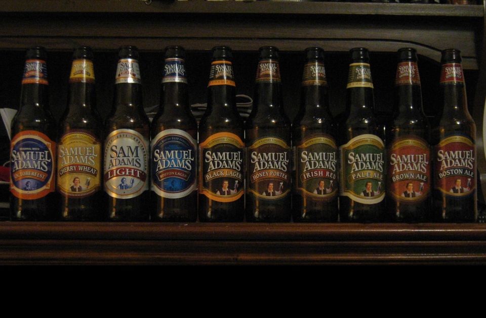 Row of ten Samuel Adams beer bottles lined up on a wooden shelf