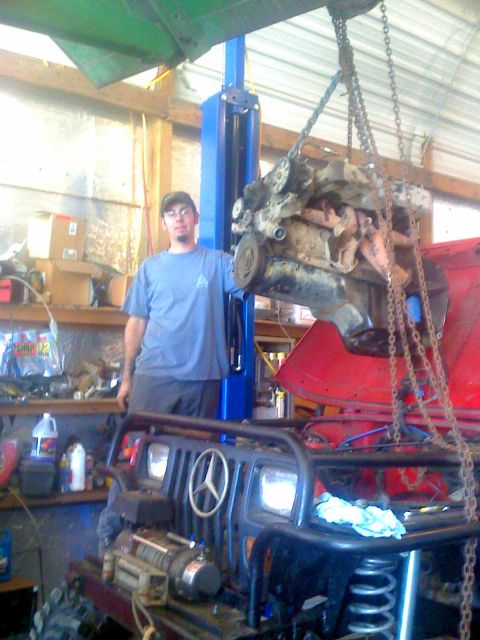1992 Ford Bronco - A man stands by a Jeep Wrangler as its engine is lifted out by a shop crane.