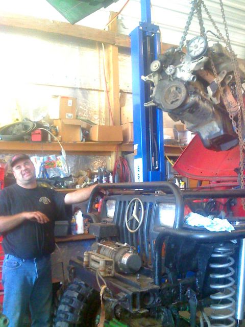 1992 Ford Bronco - Photograph of a person in a workshop next to a Jeep with a hoisted engine, not a technical document.