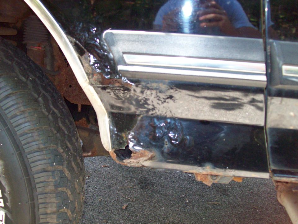 Close-up of rusted lower door and fender of a black vehicle next to a tire.