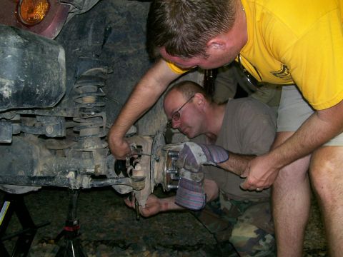 2007 Jeep Wrangler - Two men work on the suspension of a lifted Jeep Wrangler, which is supported by jack stands. One man is wearing a yellow t-shirt and the ot…