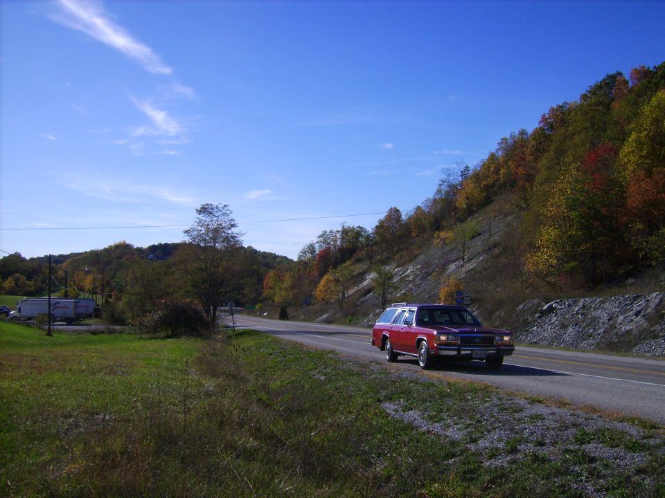 Red 1988 Ford Crown Victoria LTD station wagon driving on a road with fall colors.