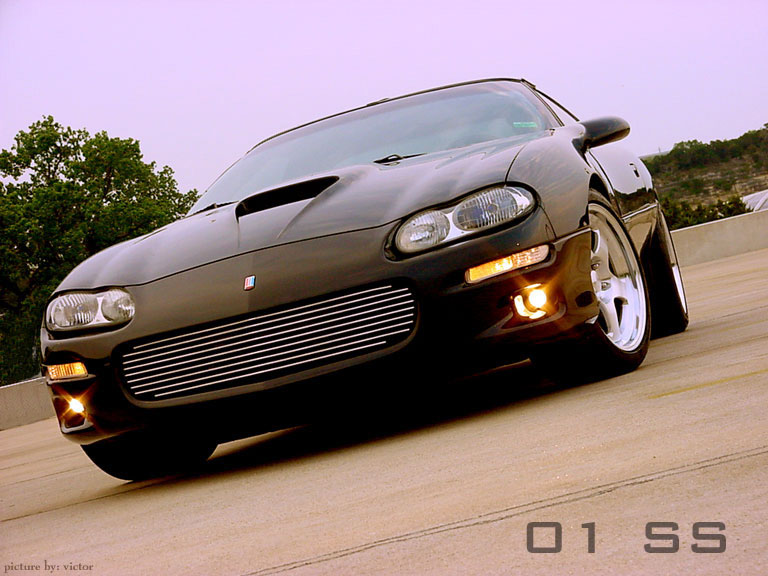 Lowered black Camaro with billet grille and fog lights on a road at dusk