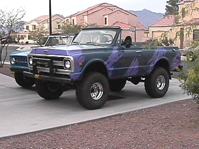 Lifted purple open-top vintage SUV with camo-style graphics and big off-road tires parked on a driveway