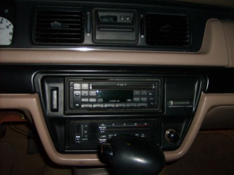 1993 Ford Crown Victoria - Interior shot of a tan and black 1990s Ford dashboard center stack, with a factory Ford cassette/CD head unit, slide-lever climate controls…