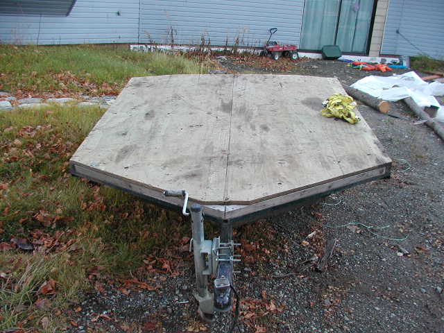 Plywood-deck flatbed utility trailer with A-frame tongue and coupler on gravel