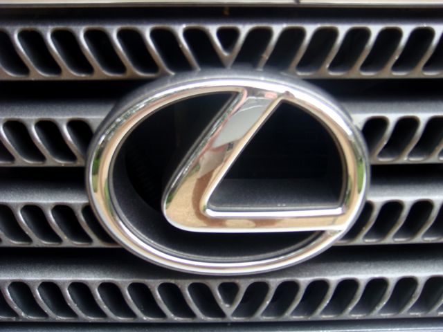 Chrome Lexus L emblem on a black slatted front grille, close-up