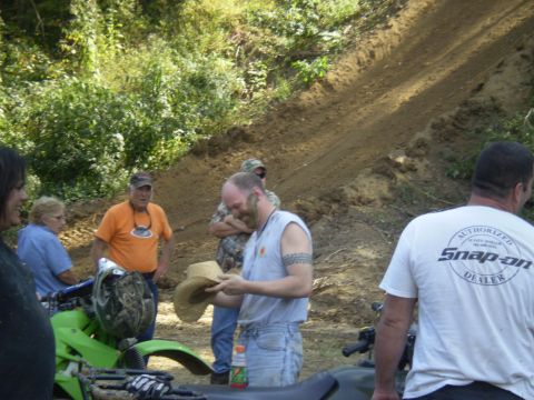 1997 Jeep Wrangler - A group of people are gathered around a bright green ATV on a dirt path, with a sandy hill in the background. One person is holding a straw…
