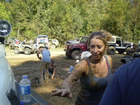 1997 Jeep Wrangler - A woman covered in mud smiles while standing in a muddy field with off-road vehicles and ATVs in the background.