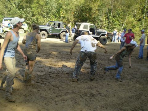 1997 Jeep Wrangler - Several people covered in mud are interacting in a muddy field with several off-road vehicles in the background. A green Jeep Wrangler is v…
