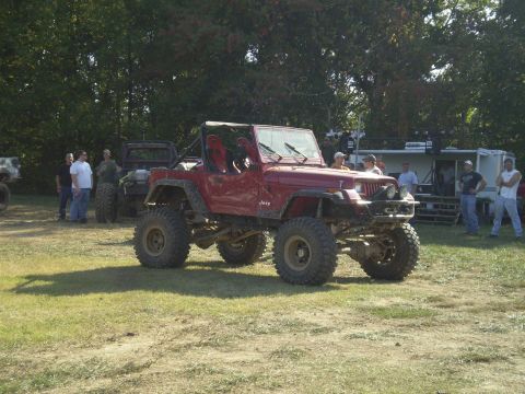 1997 Jeep Wrangler - A modified red Jeep Wrangler is parked on a grassy field with several people standing around it. The Jeep has large off-road tires and a li…