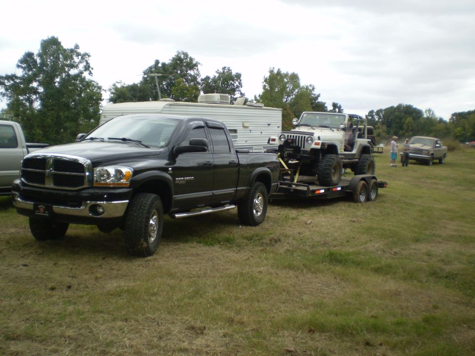Black Dodge Ram 2500 pickup truck towing a white Jeep Wrangler on a trailer.