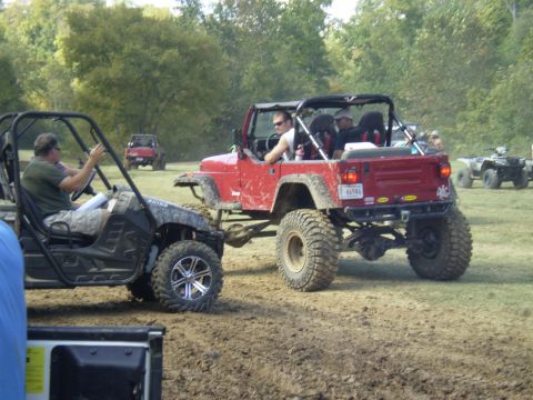 1997 Jeep Wrangler - Two off-road vehicles, a red Jeep Wrangler and a black ATV, are seen on a dirt track.