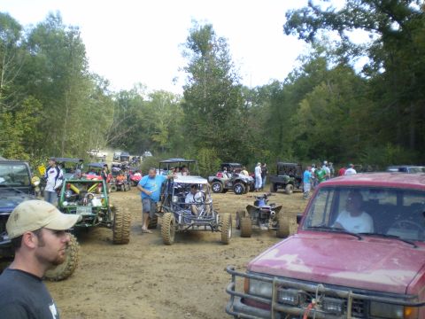 1997 Jeep Wrangler - A collection of off-road vehicles and ATVs are parked on a dirt area, with people milling around.