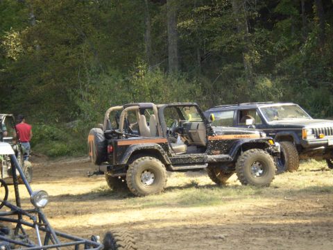 1997 Jeep Wrangler - A black 1997 Jeep Wrangler with an orange stripe is parked off-road next to another vehicle.