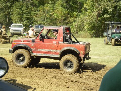 1997 Jeep Wrangler - A red Suzuki Samurai navigates a muddy track with other vehicles present.