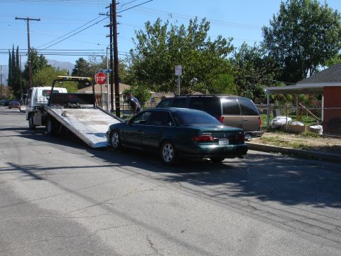 1993 Ford Taurus - A tow truck is loading a green sedan on a residential street.
