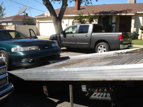 1993 Ford Taurus - A green sedan is loaded onto a flatbed tow truck, with a gray pickup truck visible in the background.