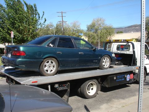 1993 Ford Taurus - A dark green 1993 Ford Taurus sedan is loaded onto a tow truck.
