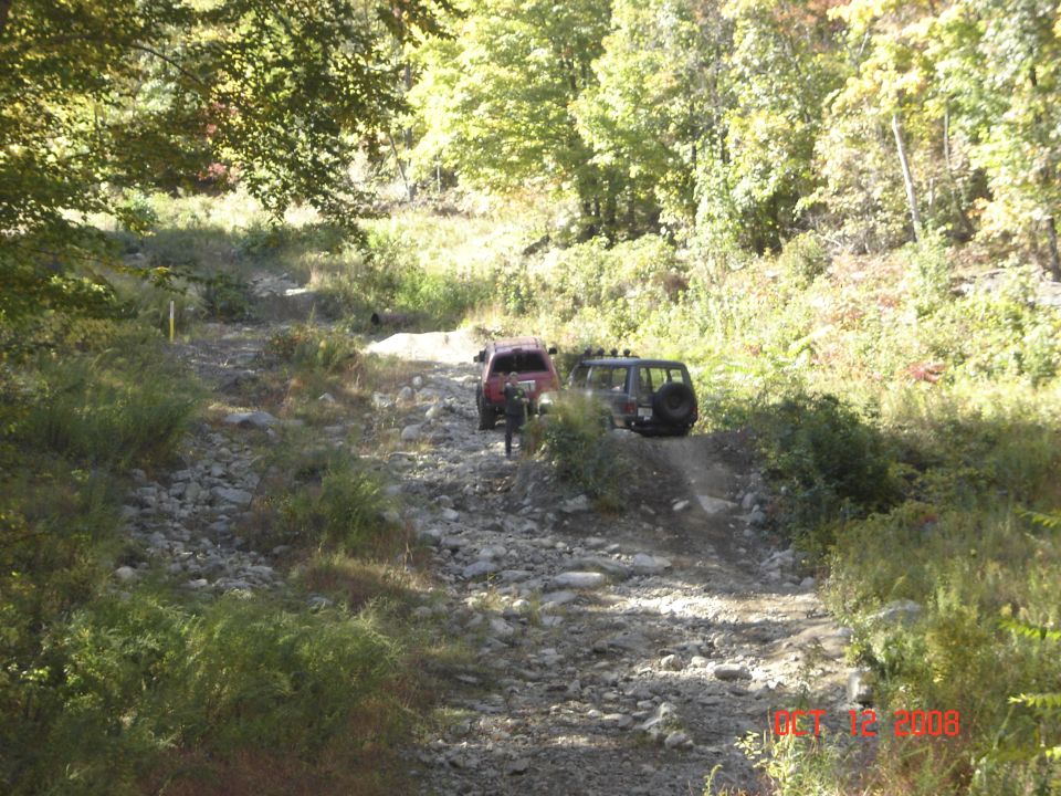 Red Jeep Cherokee and green Jeep Wrangler on a rocky wooded off-road trail
