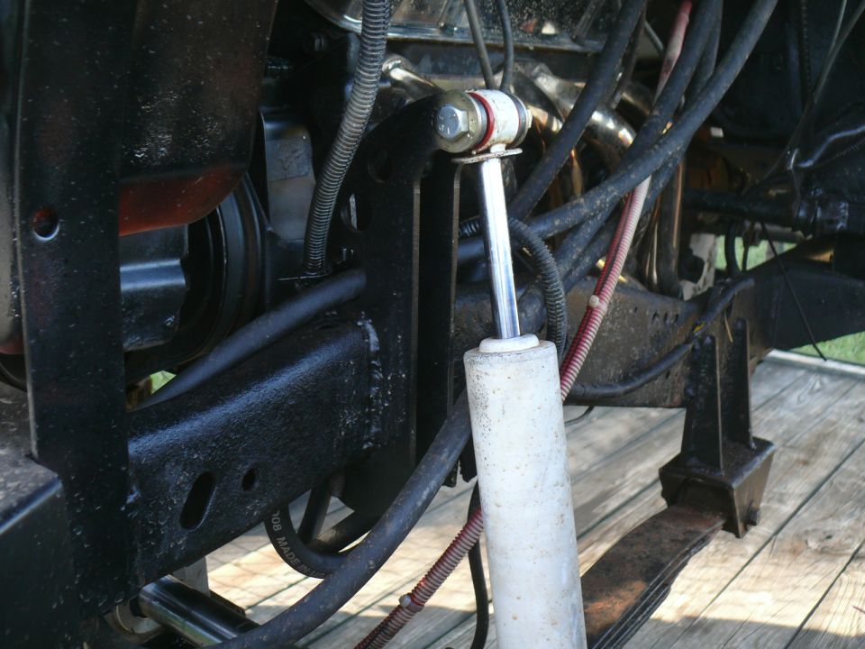 Close-up of a white shock absorber and leaf spring assembly with black metal brackets and wiring