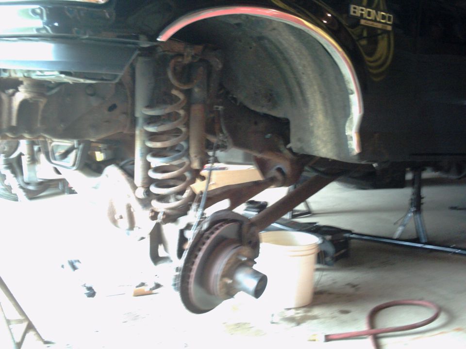 close-up of vehicle's front suspension and brake assembly, with a bucket nearby